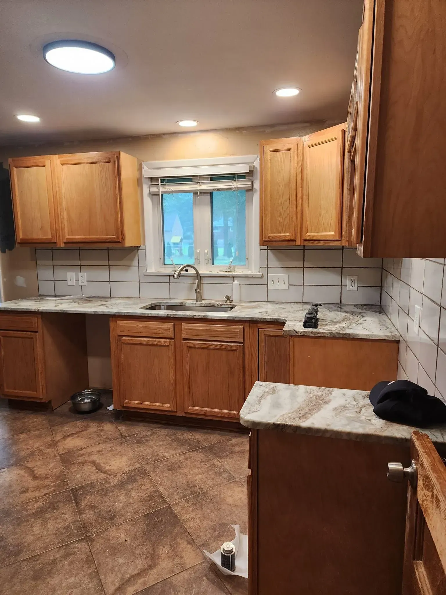 A kitchen with wooden cabinets , granite counter tops , a sink and a window.