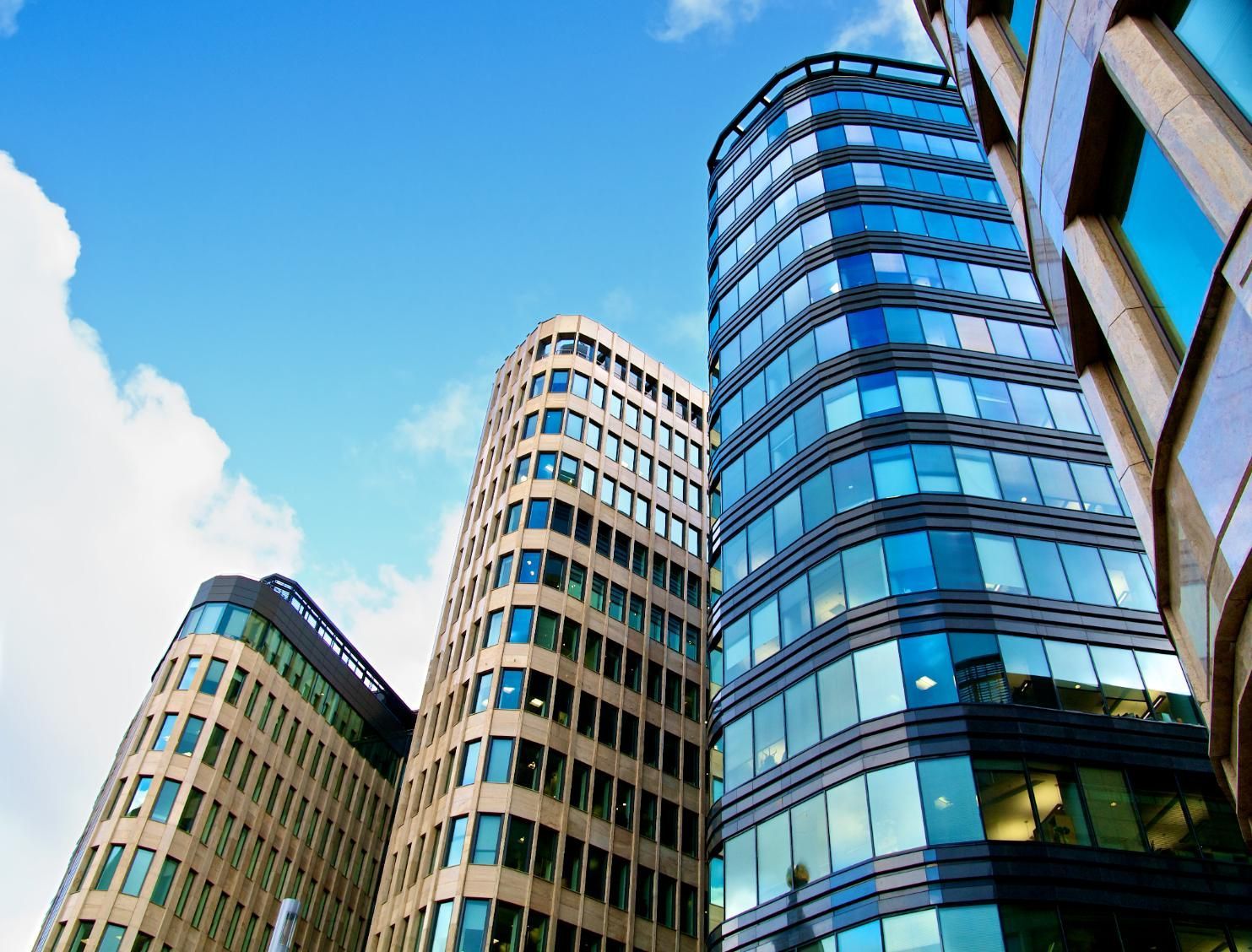 Modern office buildings with blue glass windows against a blue sky with clouds.