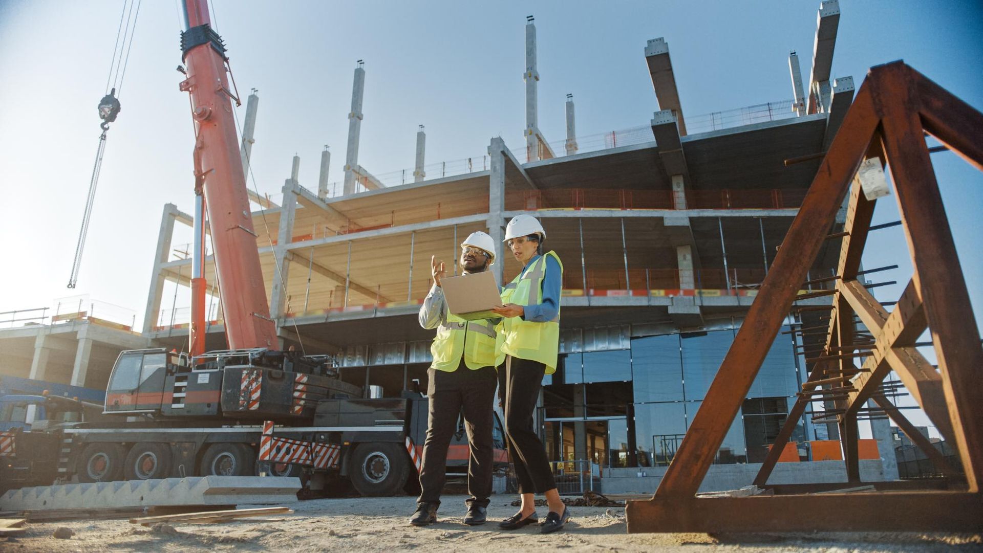 Construction workers reviewing blueprints on a building site, crane in background.