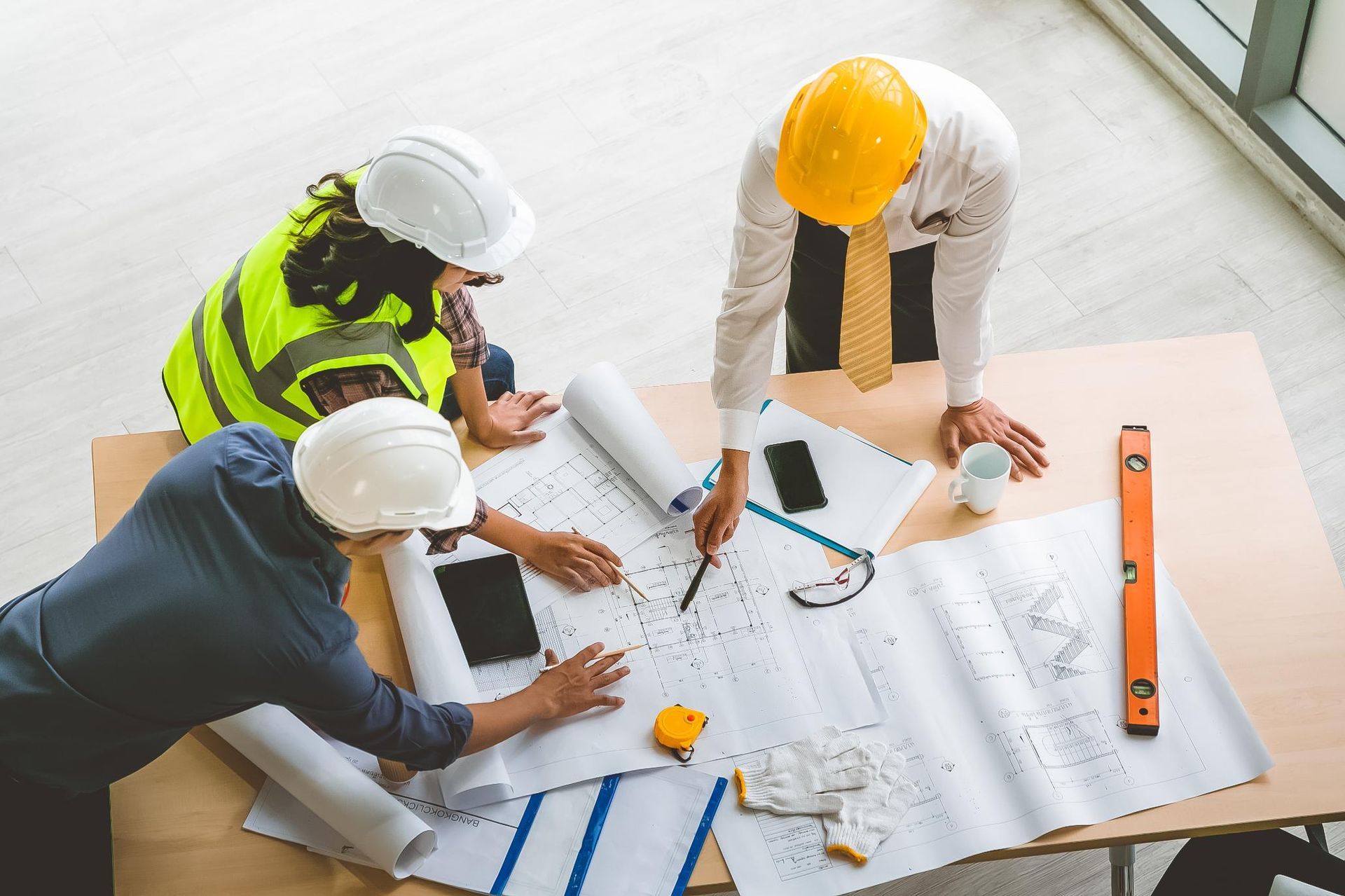 Three construction workers in hard hats reviewing blueprints at a table.