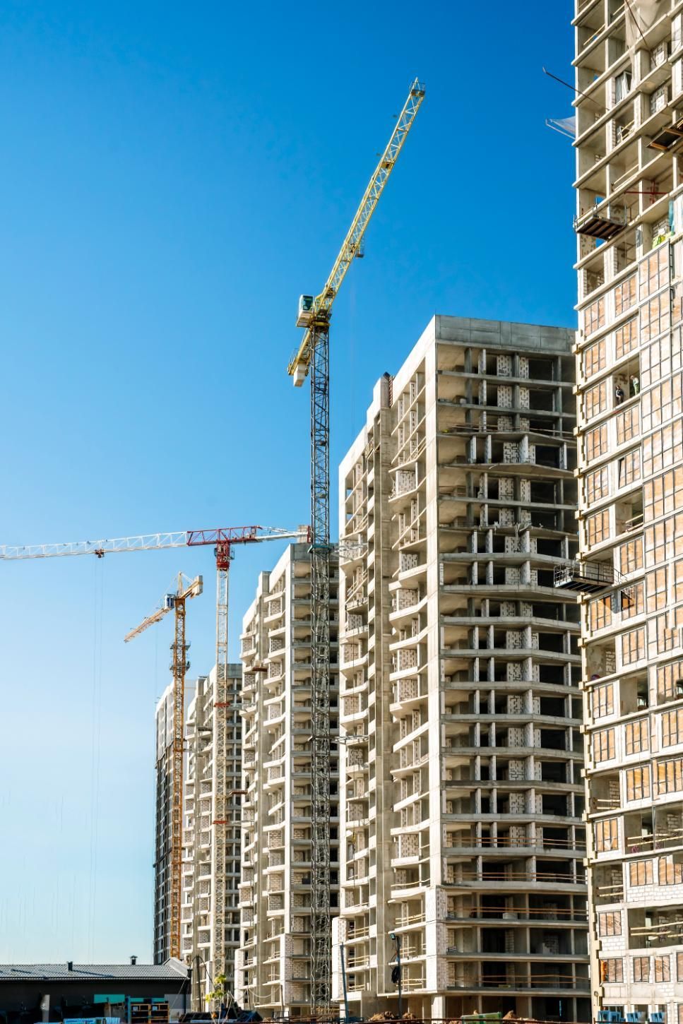 Construction of several high-rise buildings with cranes against a bright blue sky.