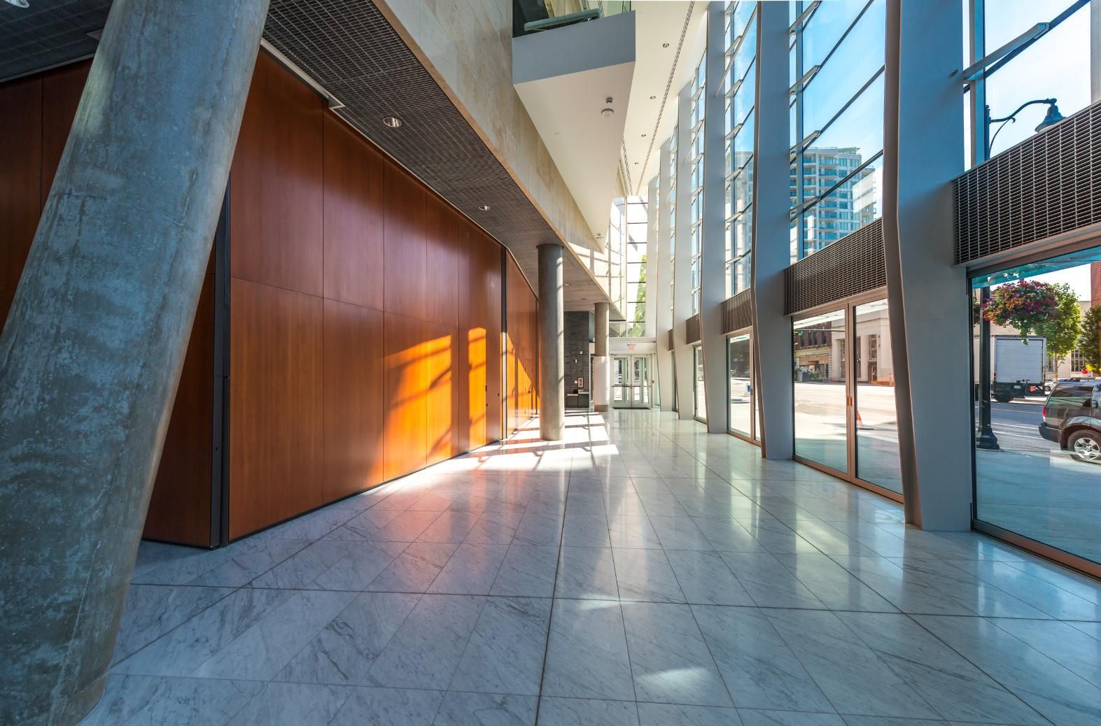 Long hallway with marble floors, floor-to-ceiling windows, and a wooden wall. Sunlight streams in.