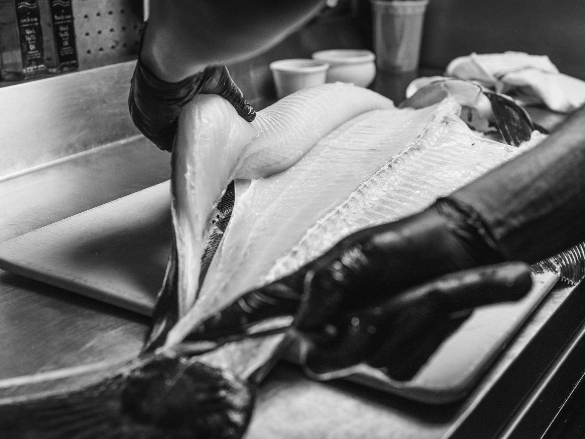 A black and white photo of a person cutting a fish on a cutting board.