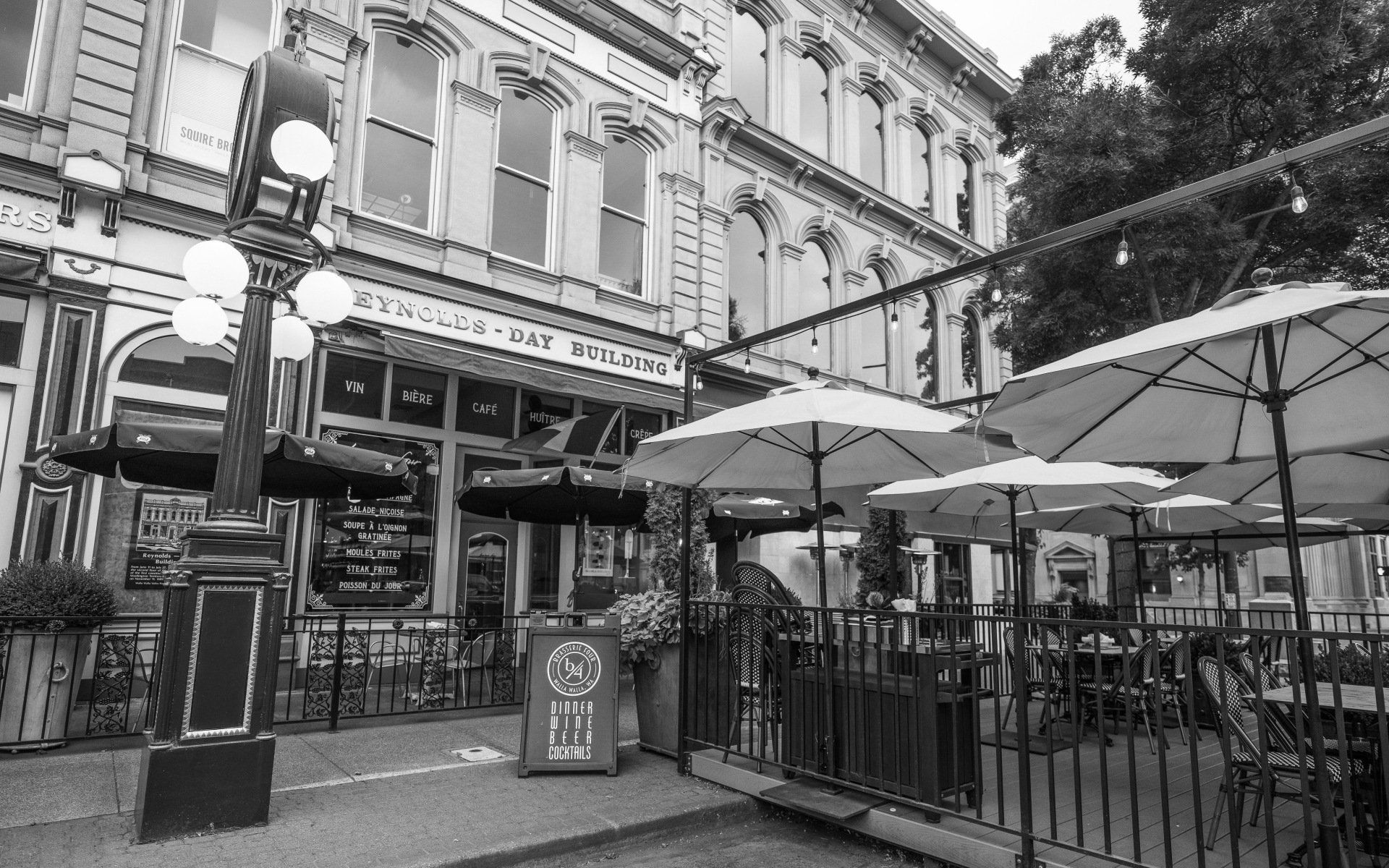 A black and white photo of a restaurant with umbrellas and chairs outside.
