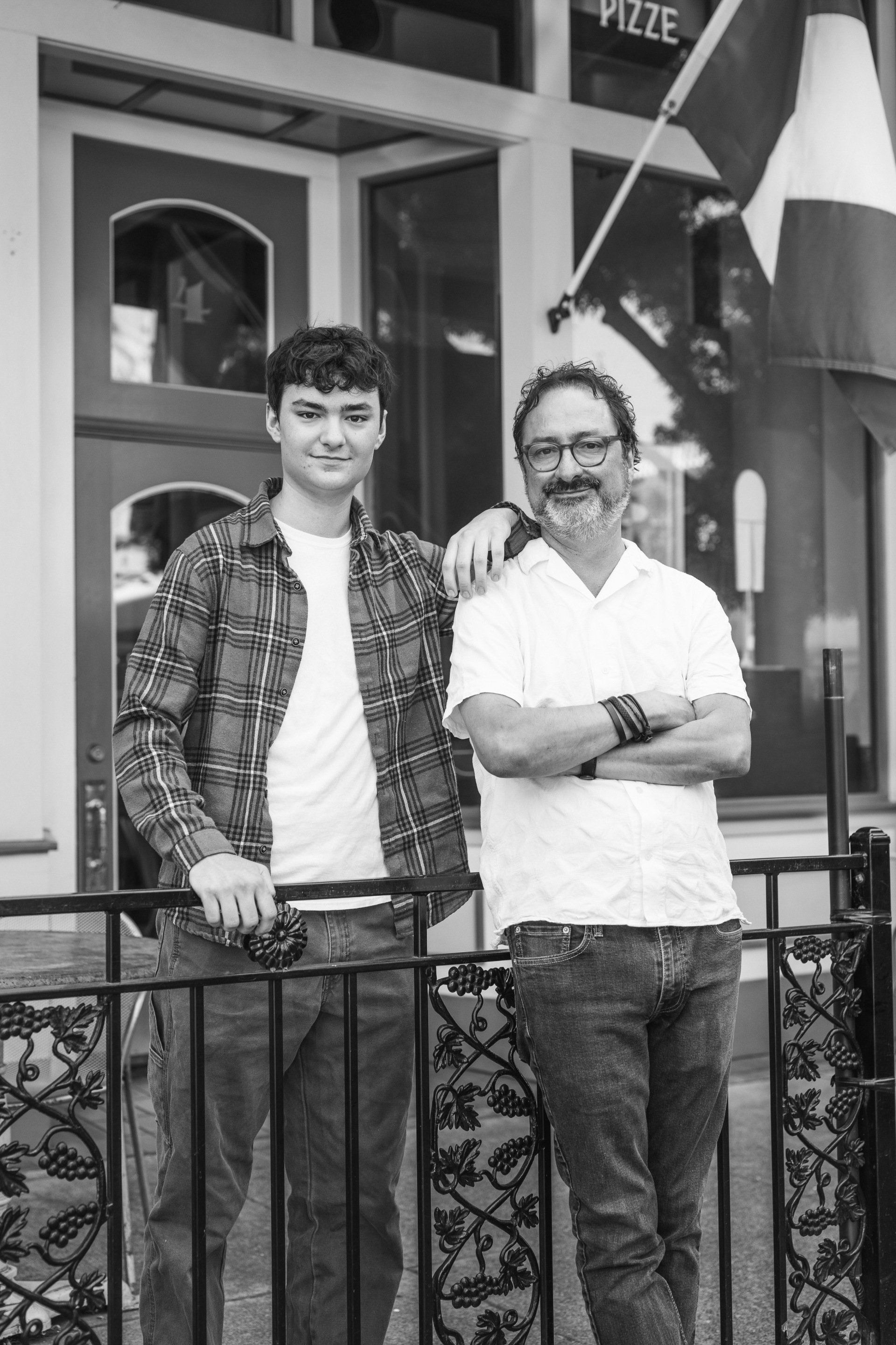 Two men are standing next to each other on a balcony in front of a building.