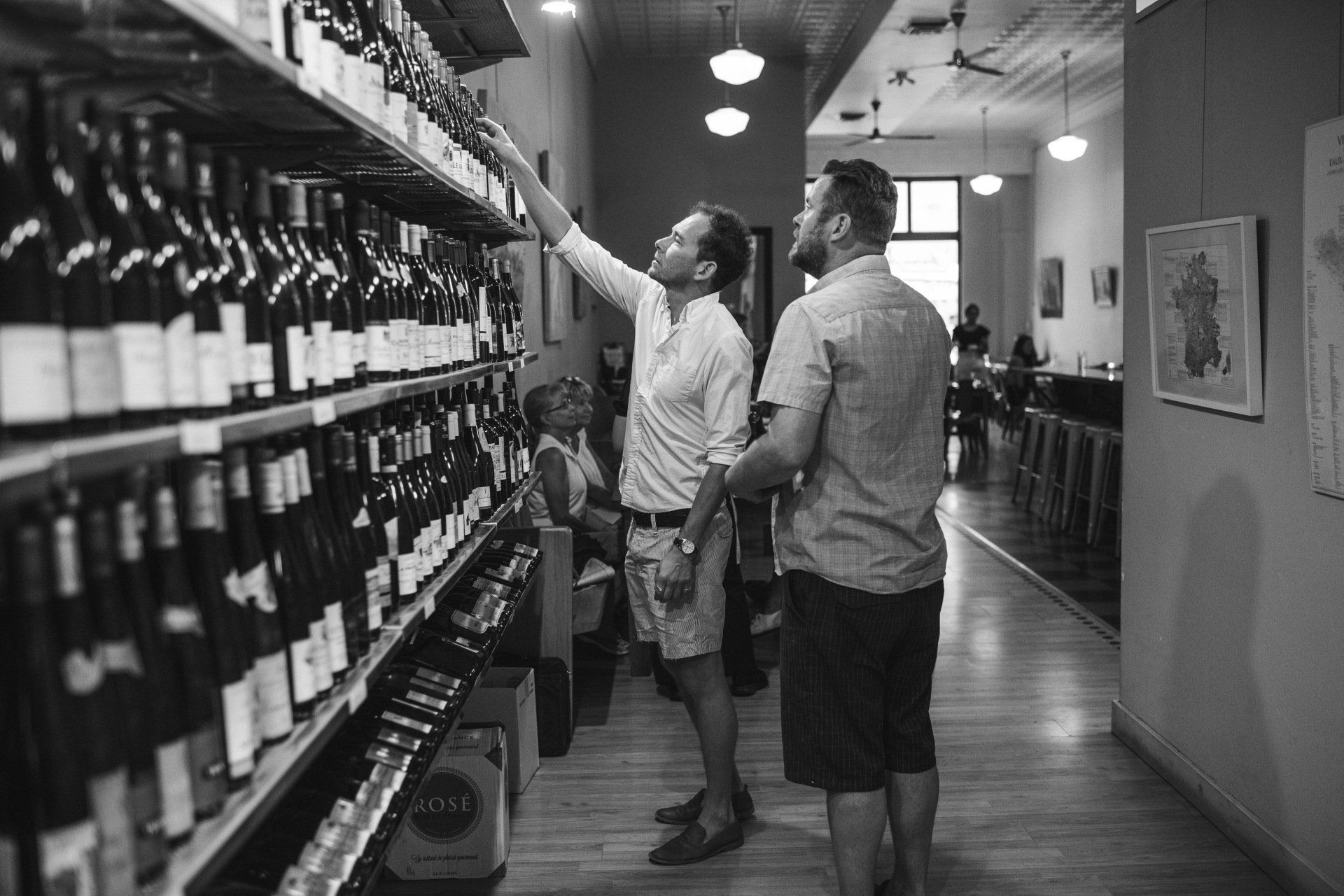 Two men are looking at wine bottles on shelves in a store.