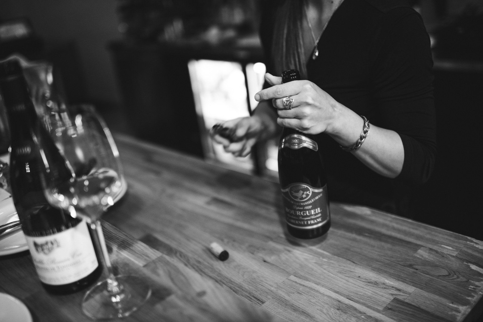 A woman is opening a bottle of wine on a wooden table.