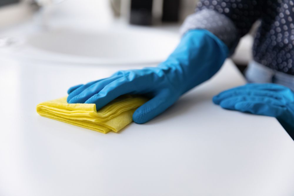 A Person Wearing Blue Gloves Is Cleaning a Counter with A Yellow Cloth — Haydyn's Cleaning In Urraween, QLD