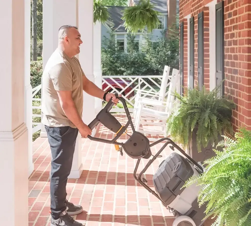 A person pushing a portable floor cleaner across a brick porch.