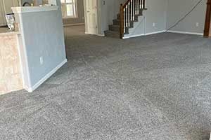 An interior room with gray carpet, a partial wall, and a staircase leading to an upper level.