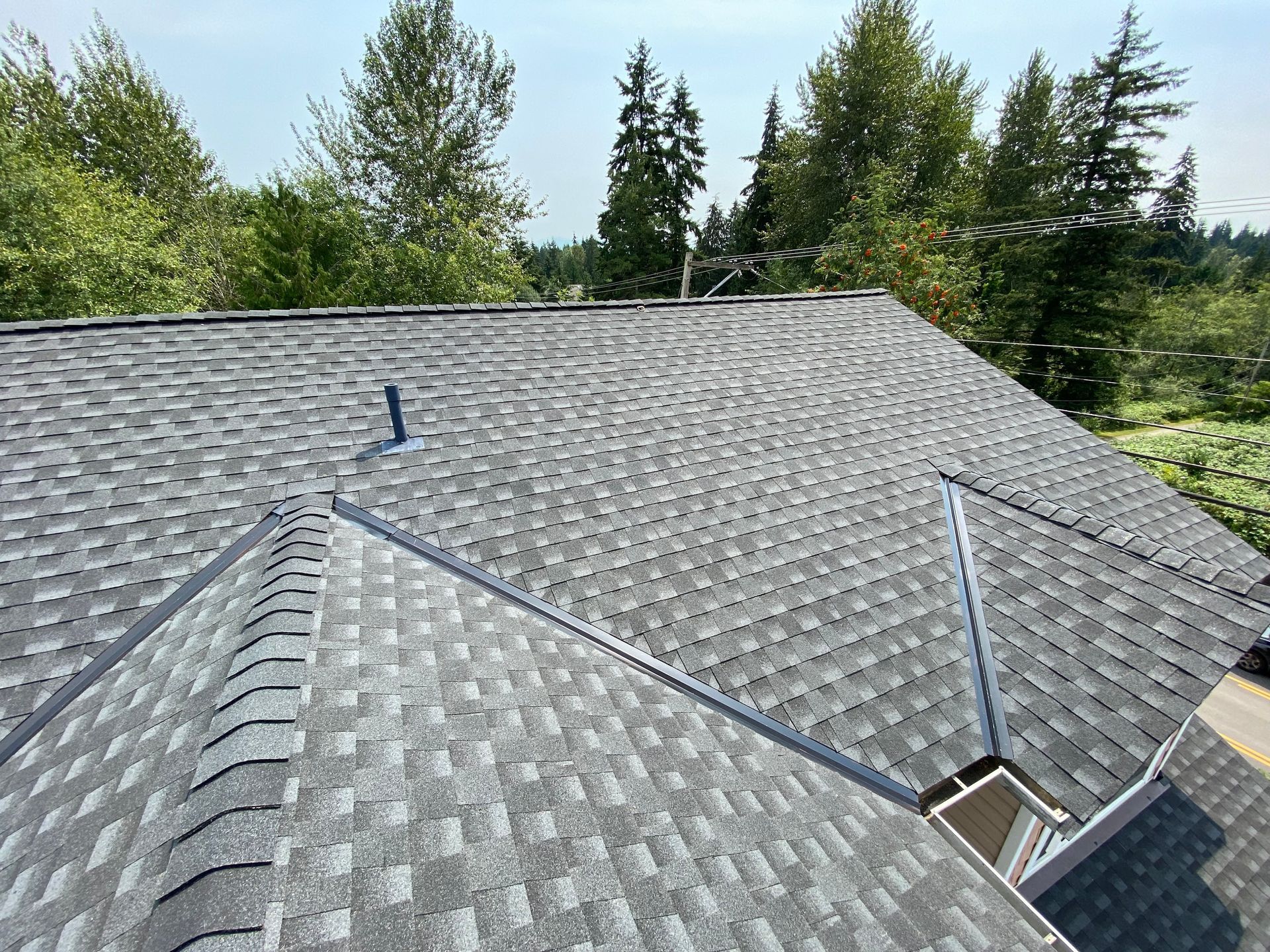 Gray asphalt shingle roof with metal flashing on a house, surrounded by trees.