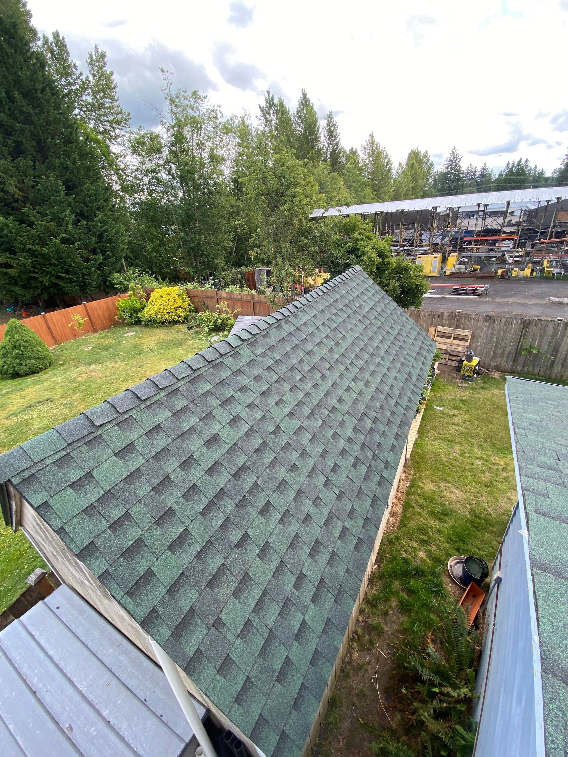 Green shingle roof on a shed, viewed from above, with trees and a yard visible in the background.