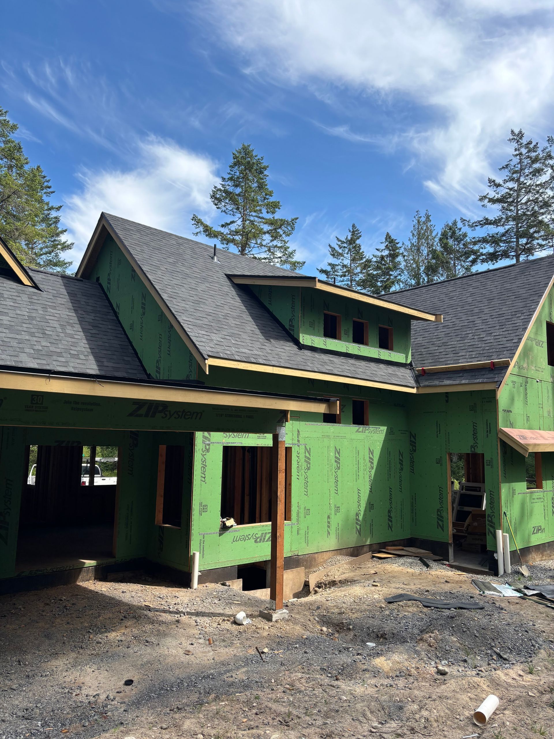 House under construction, green sheathing, dark roof, windows, outdoors, blue sky.