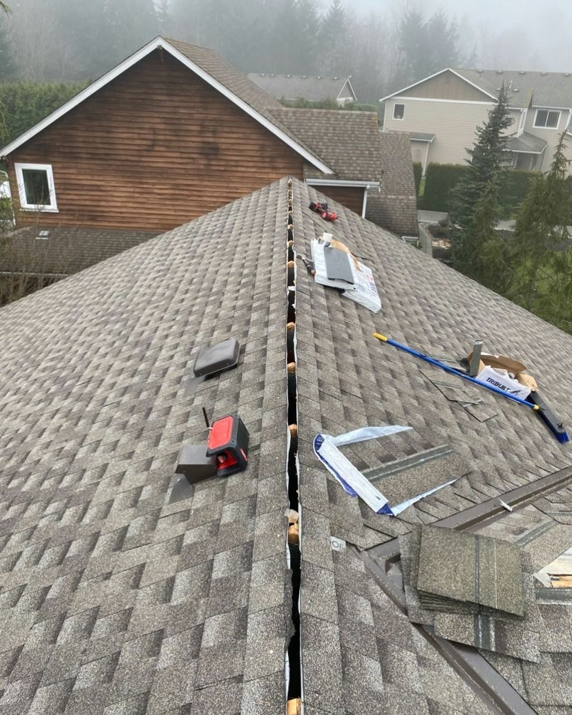 View of a gray shingle roof being worked on, tools and materials visible on the ridge.