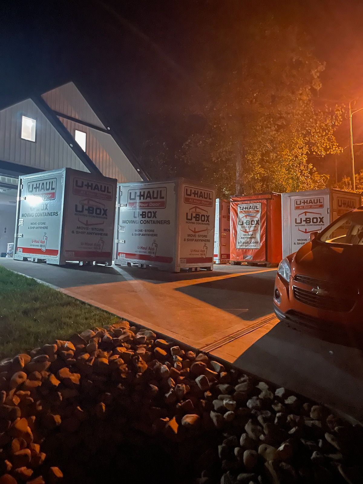 U-Haul moving containers parked in front of a building at night. A car is visible on the right.