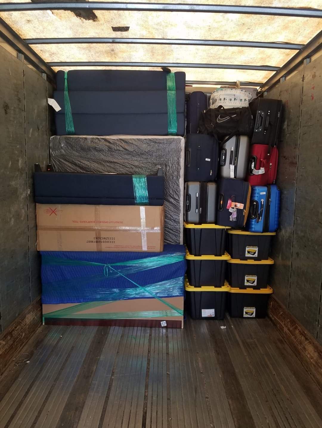 Moving truck interior packed with furniture, boxes, and bins, secured with straps.