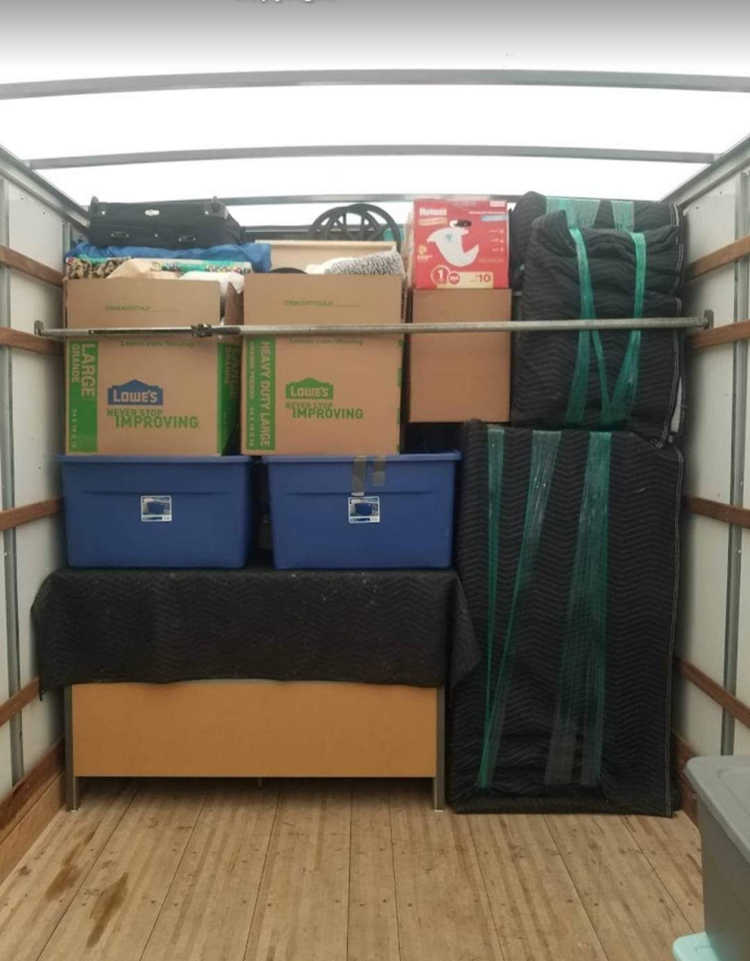 A cargo truck interior is filled with packed boxes, containers, and furniture, secured with straps.