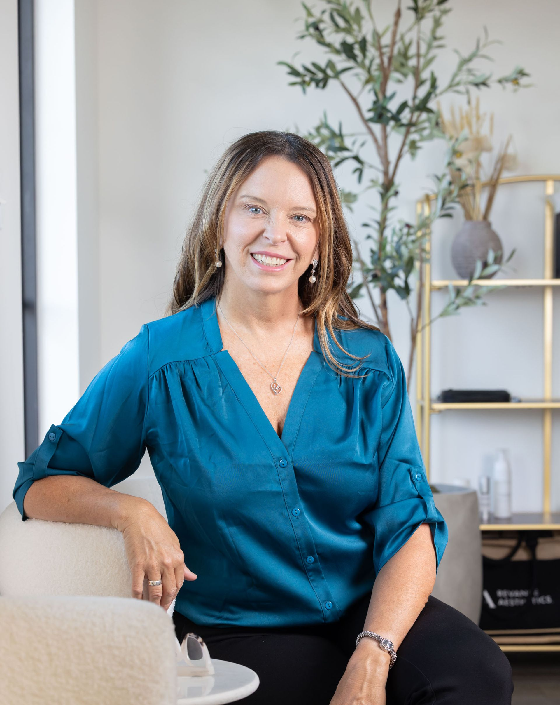 A woman wearing a sweater and a heart necklace is smiling at the camera.