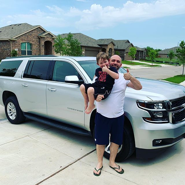 A man is holding a little boy in front of a silver suv