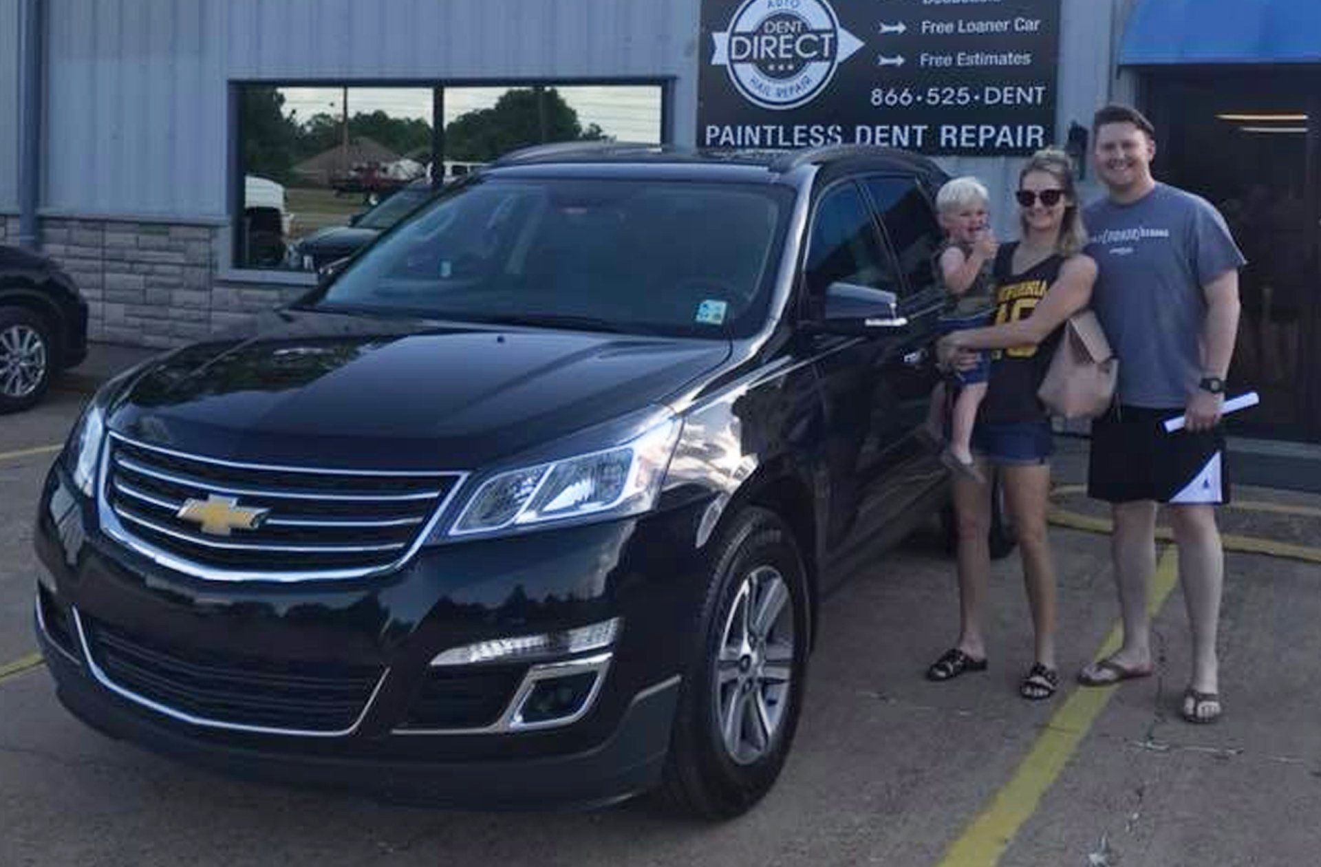 A family is standing in front of a black car in a parking lot.