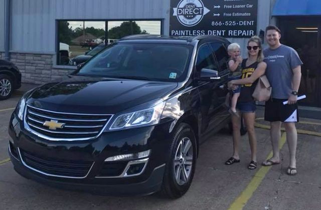A family standing in front of a black chevrolet suv