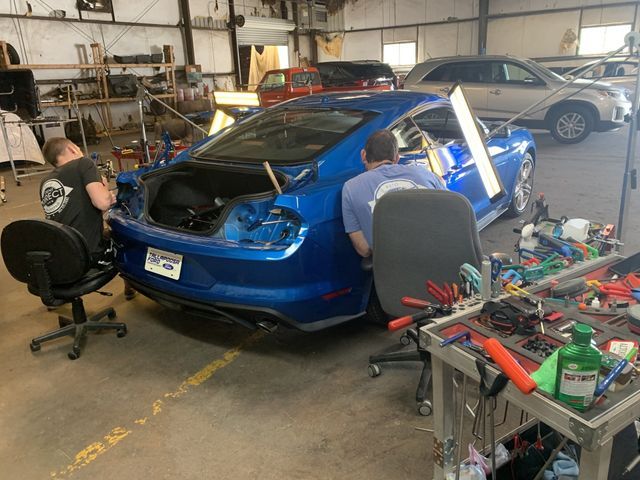 Two men are working on a blue car in a garage