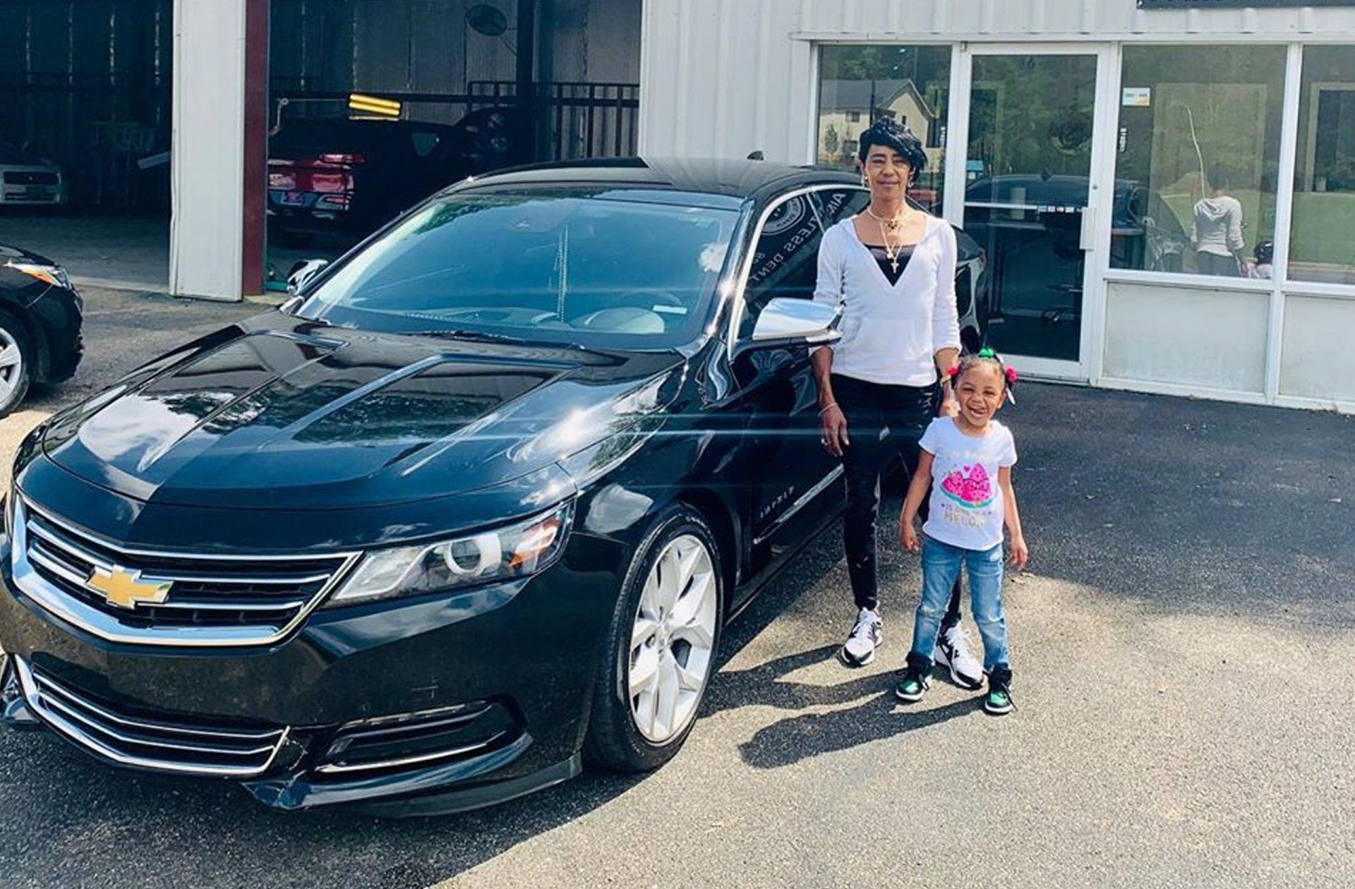 A woman and a child are standing in front of a black car.