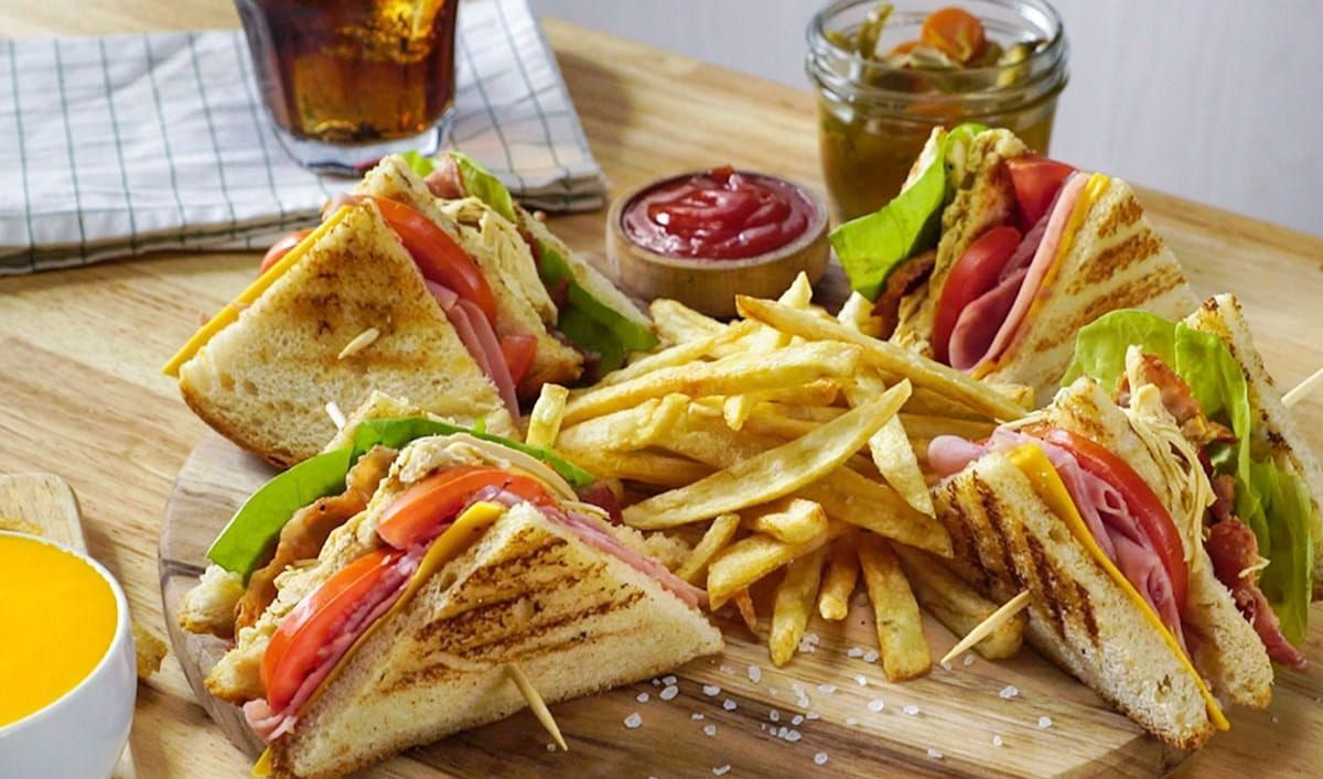 A club sandwich and french fries on a wooden cutting board.