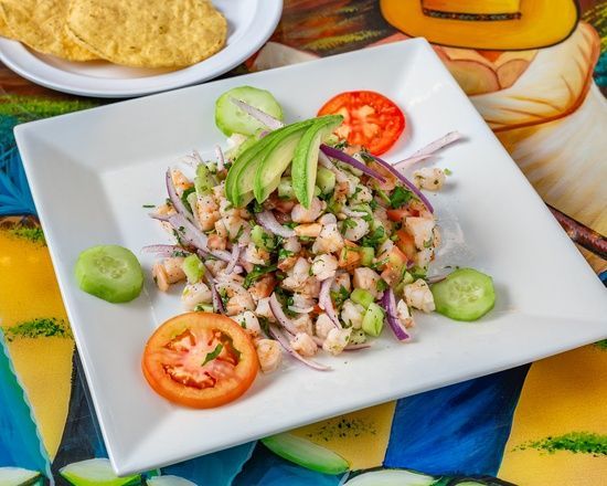 A white plate topped with shrimp , tomatoes , cucumbers and avocado.