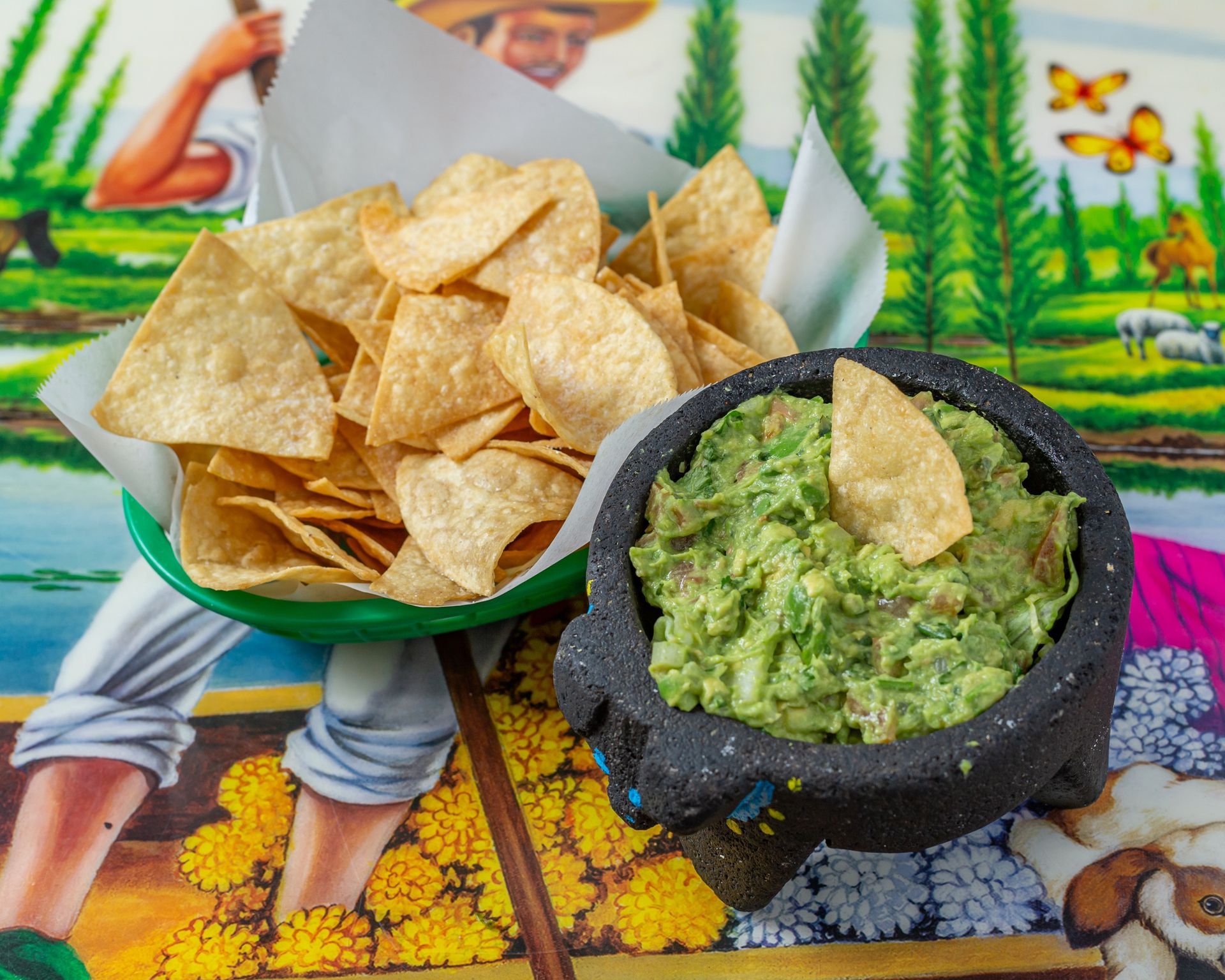A bowl of guacamole next to a bowl of tortilla chips.