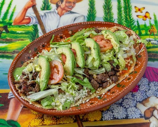 A plate of food with avocado , tomatoes , lettuce and meat on a table.