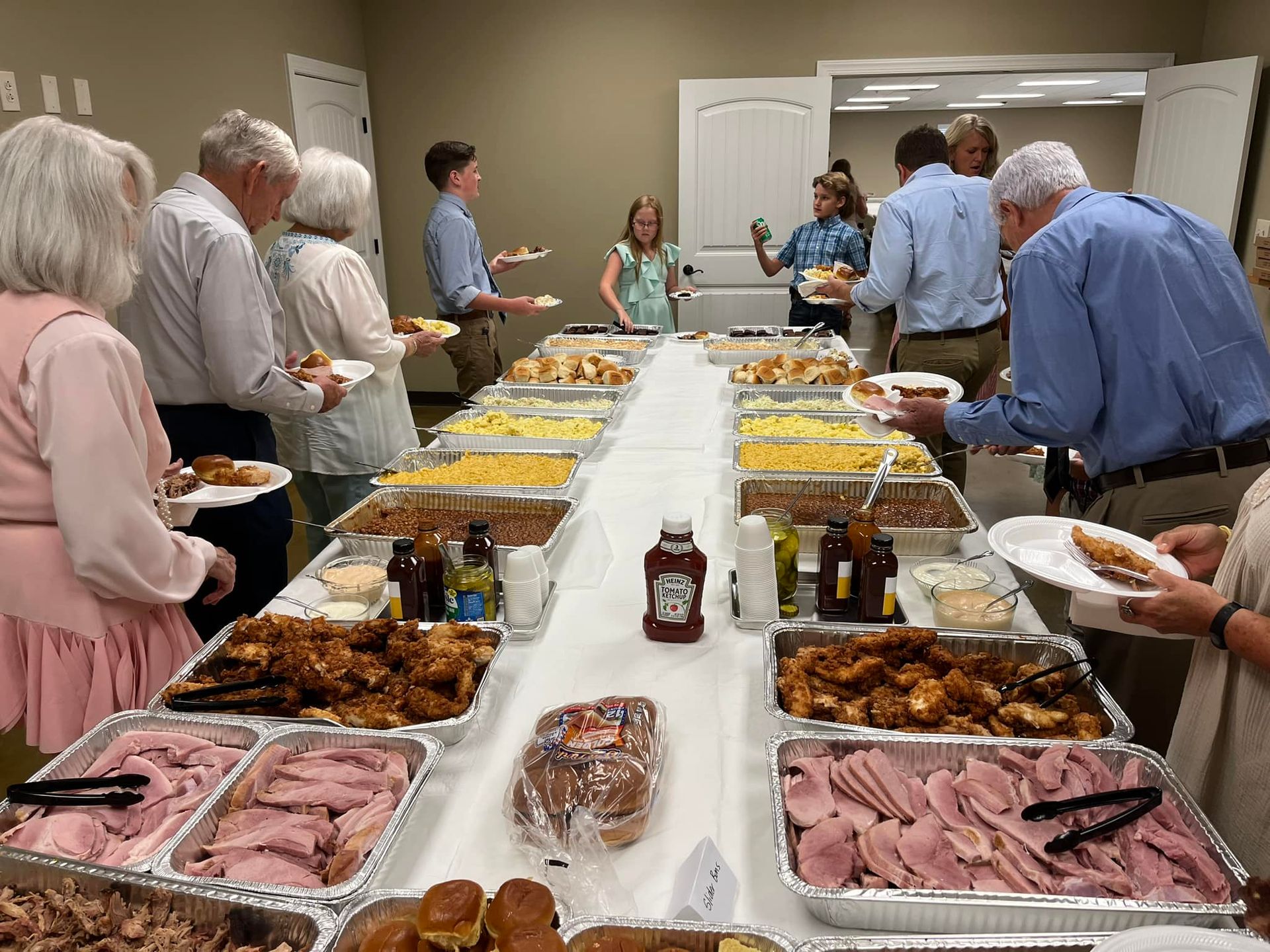 A group of people are standing around a long table filled with food.