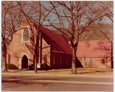 A church with a red roof is surrounded by trees