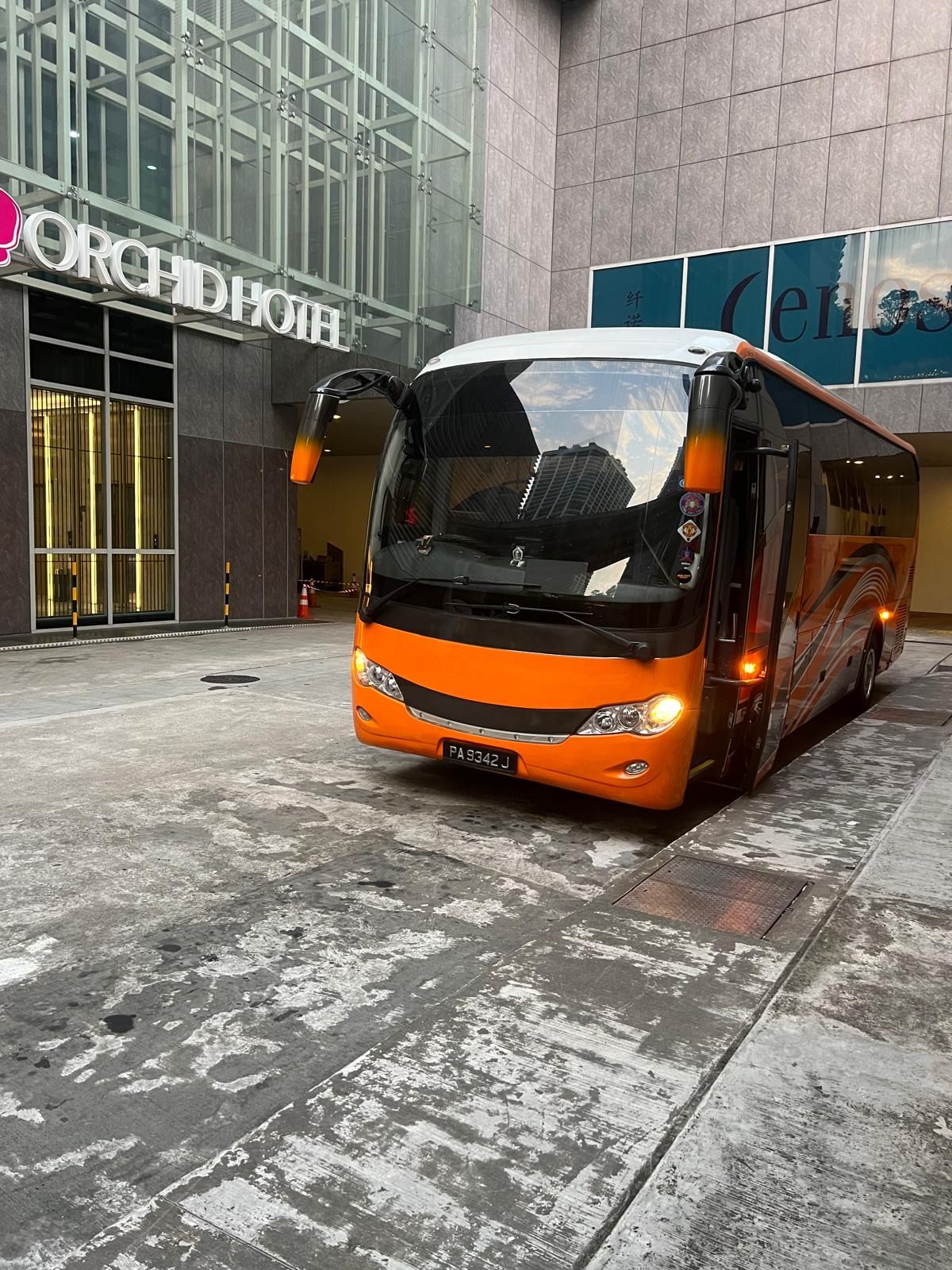 Orange bus parked outside the Orchard Hotel with a building entrance in Singapore.