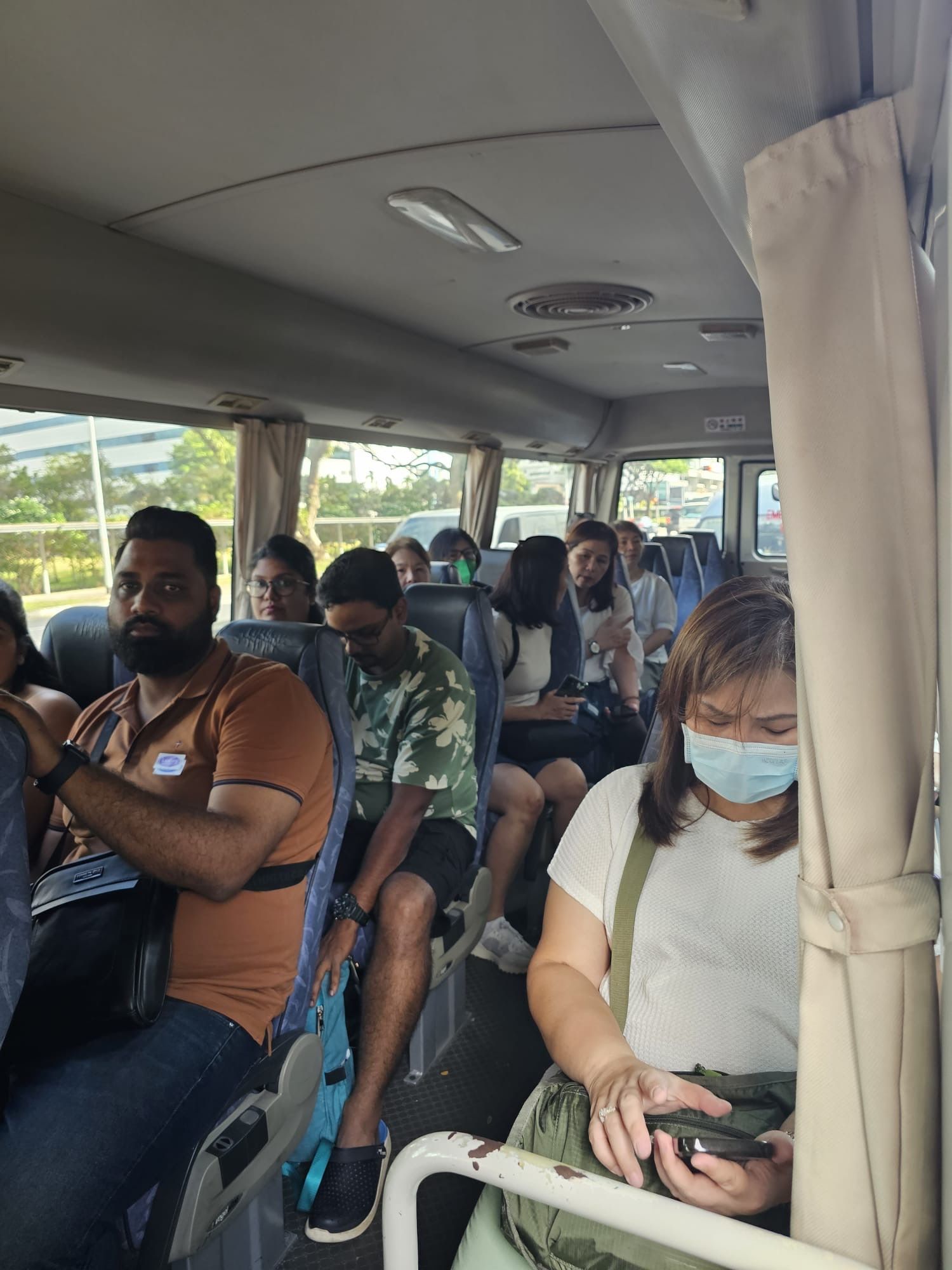 People inside a bus, some wearing masks, traveling; interior view with seats, curtains.