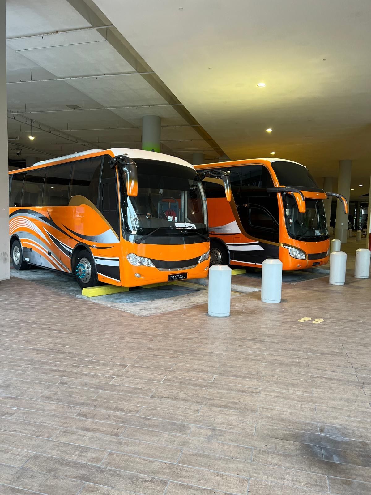 Two orange and black tour buses parked indoors.