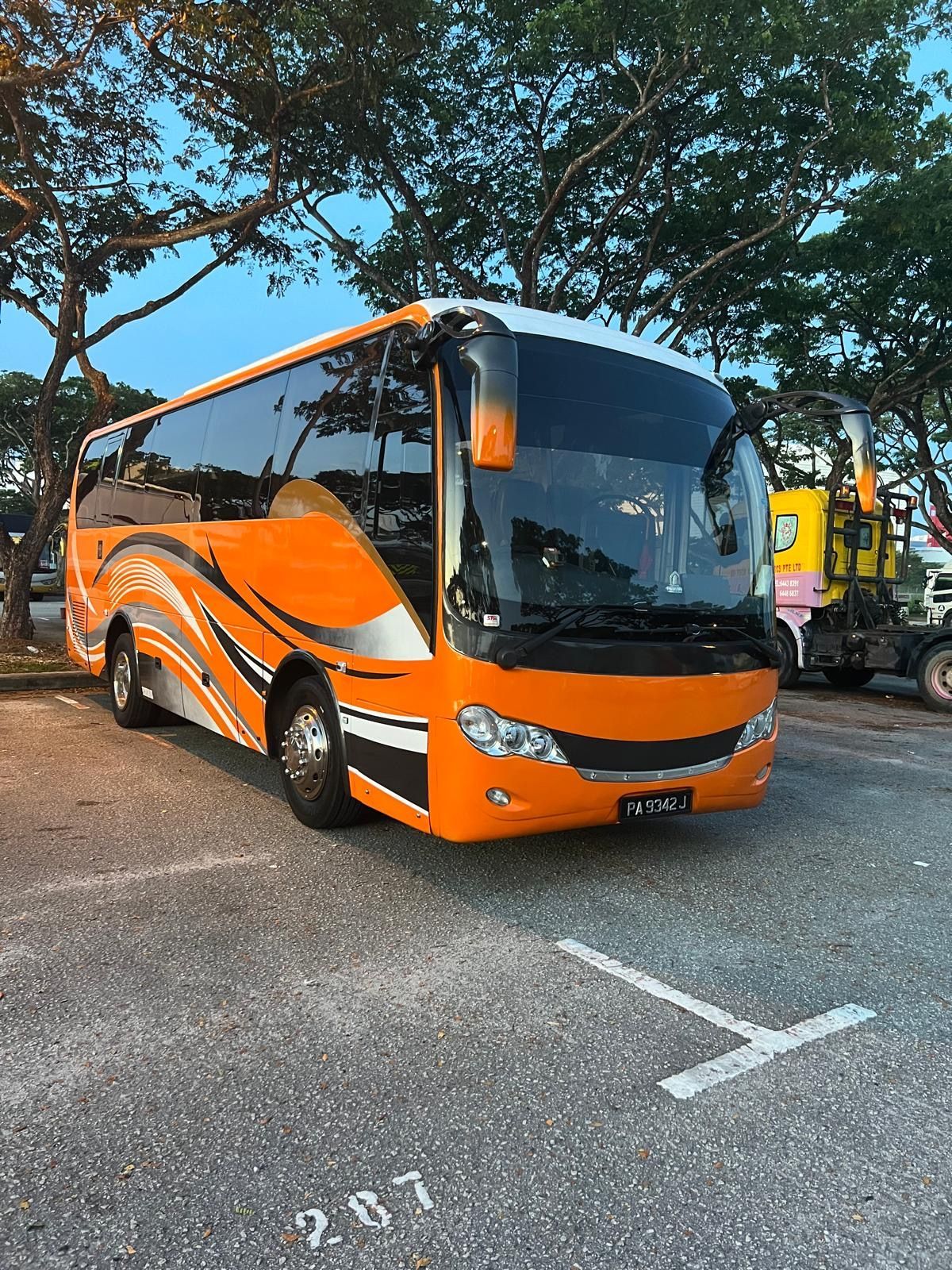 Orange tour bus parked in a lot, with black and white stripes.