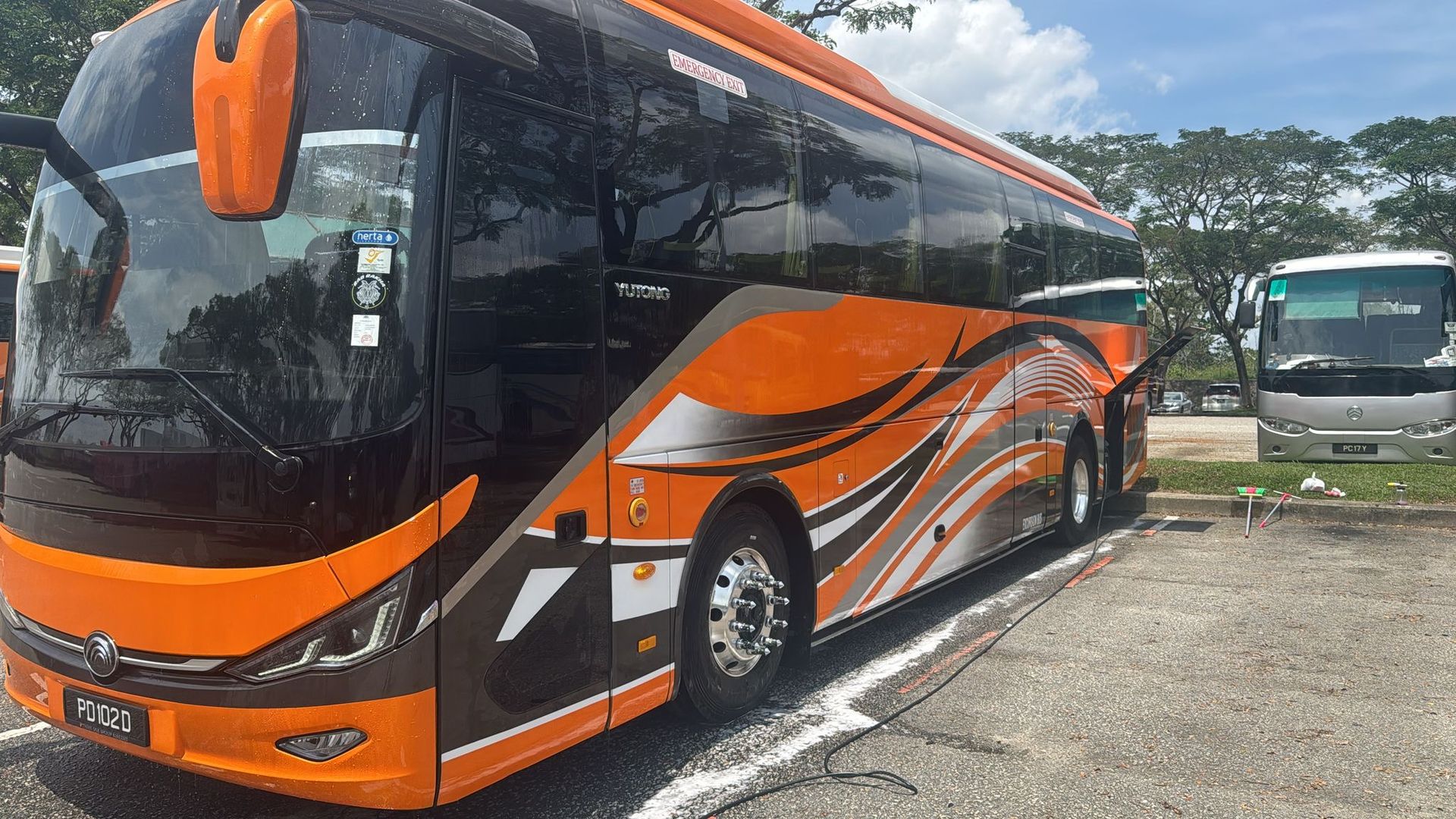 Orange and black coach bus parked in a lot, other buses in background.