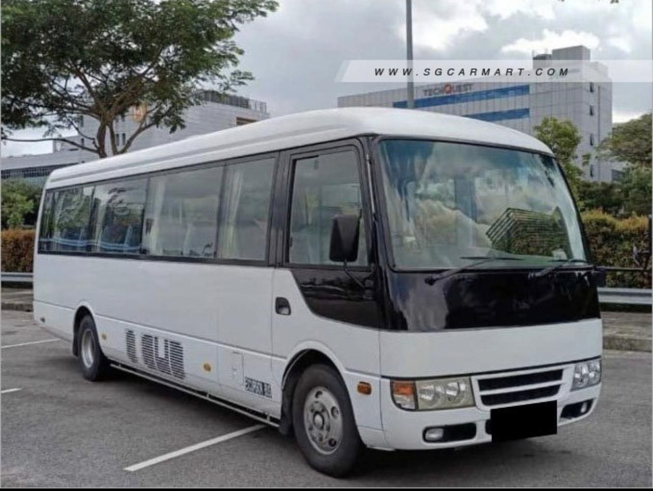 White bus parked on asphalt; front view, black accents, buildings in background.