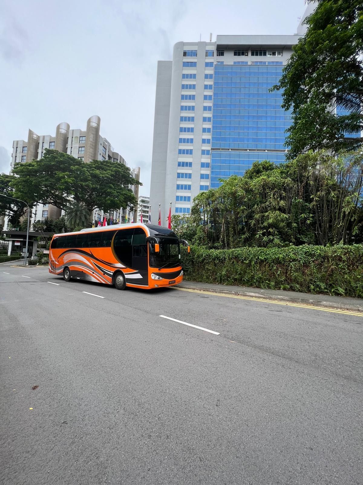 Orange bus on a city street, with a tall glass building in the background.