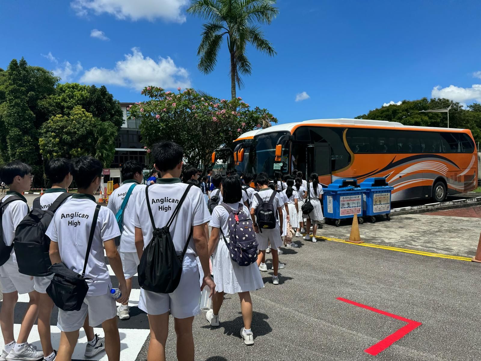 Students in white uniforms boarding an orange bus on a sunny day.