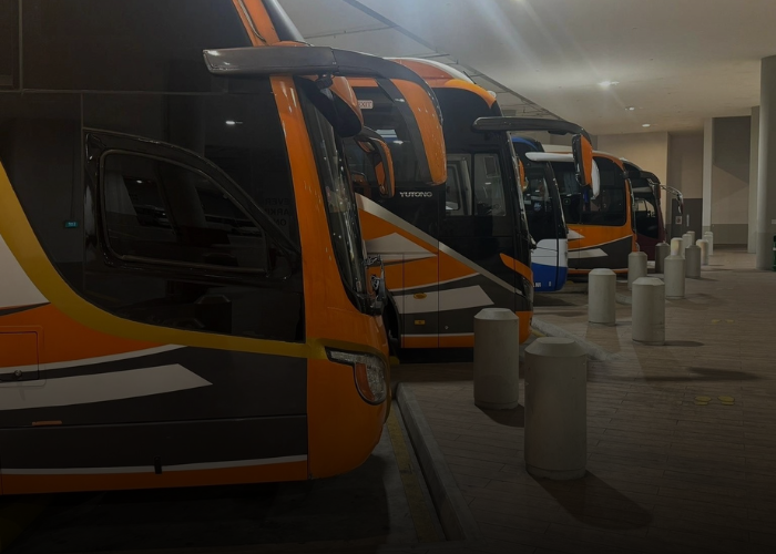 Several orange and black buses parked at a loading area, illuminated by ambient lighting.