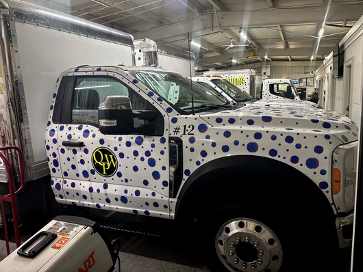 White truck with blue polka dots, parked in a garage. It has a logo on the door and