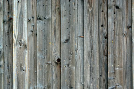 Weathered wooden planks, vertical grain, gray tones, knots, and nail holes visible.
