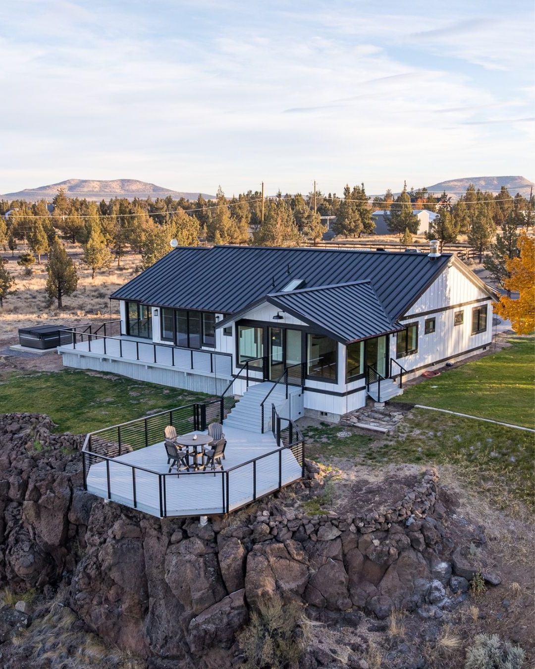 Modern white house with dark roof and large windows, perched on a rocky cliff overlooking a landscape.