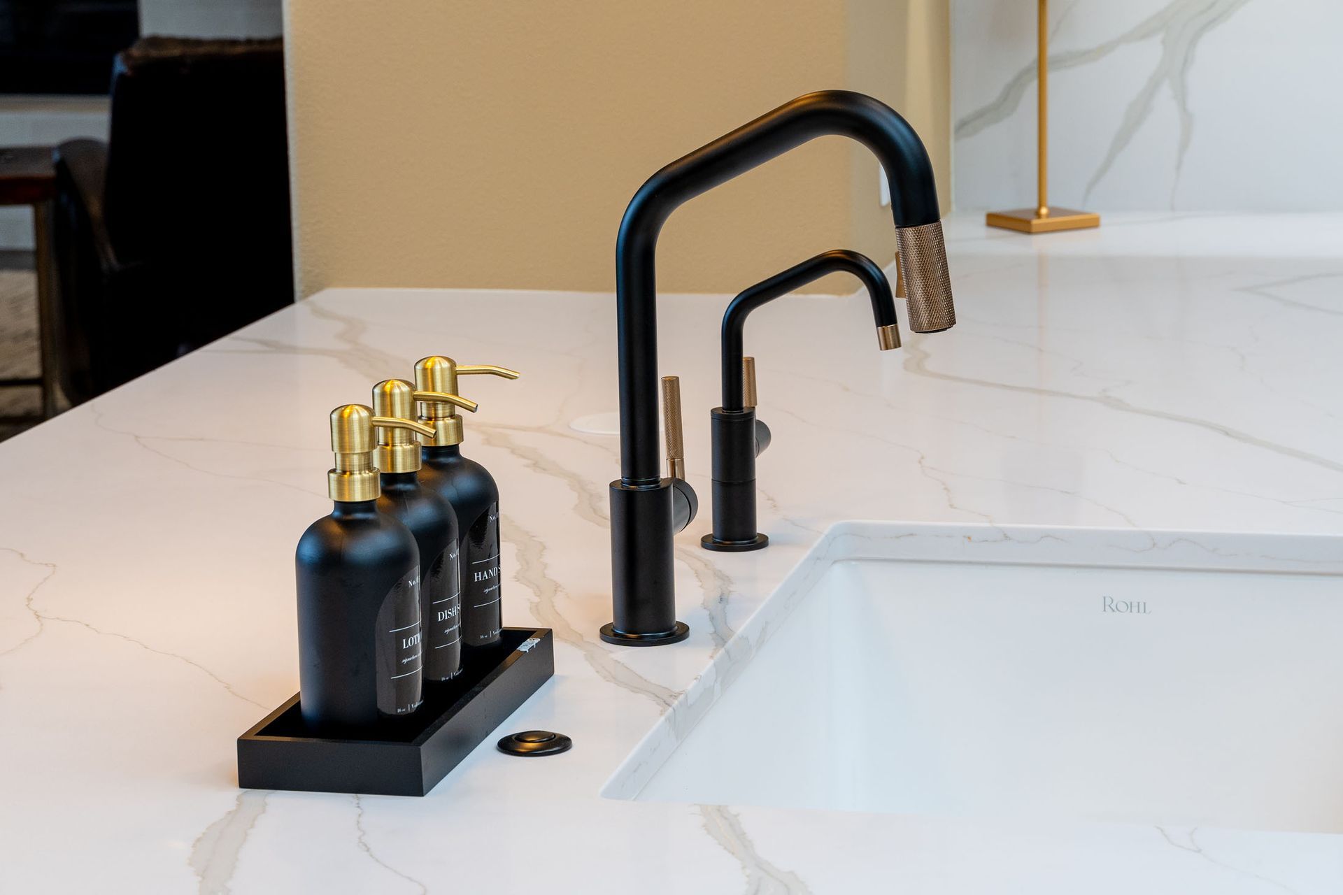 A kitchen sink with two black faucets and three black bottles on a tray.