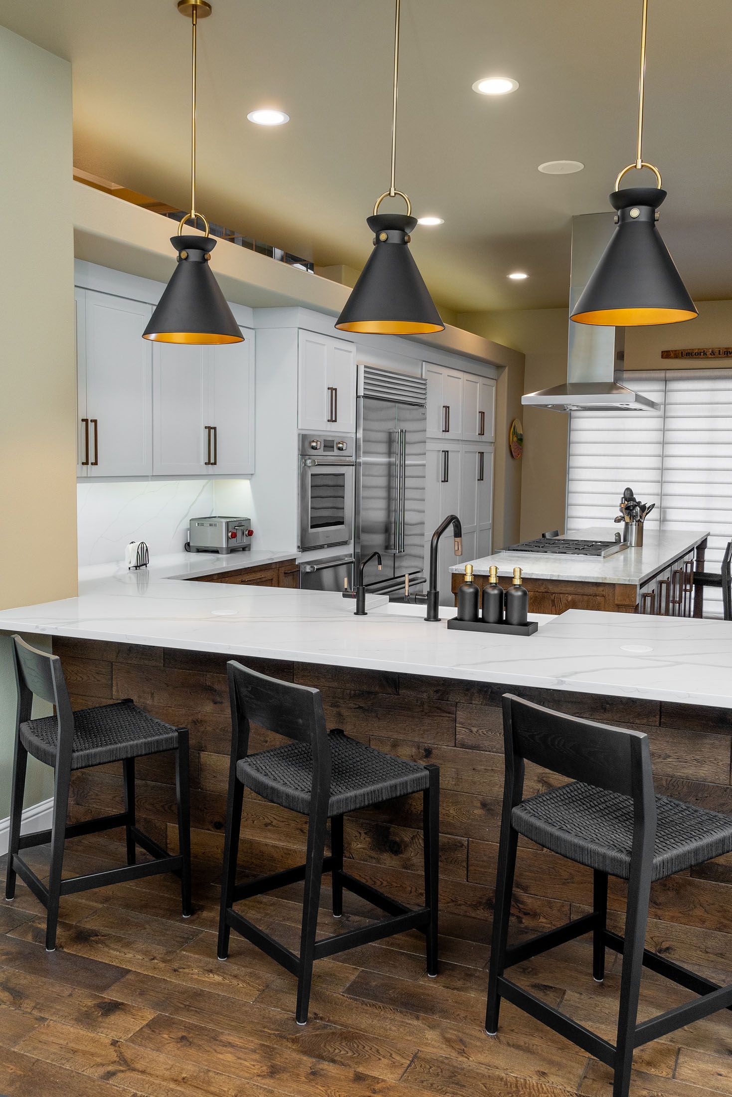 A kitchen with a large island , stools and pendant lights.