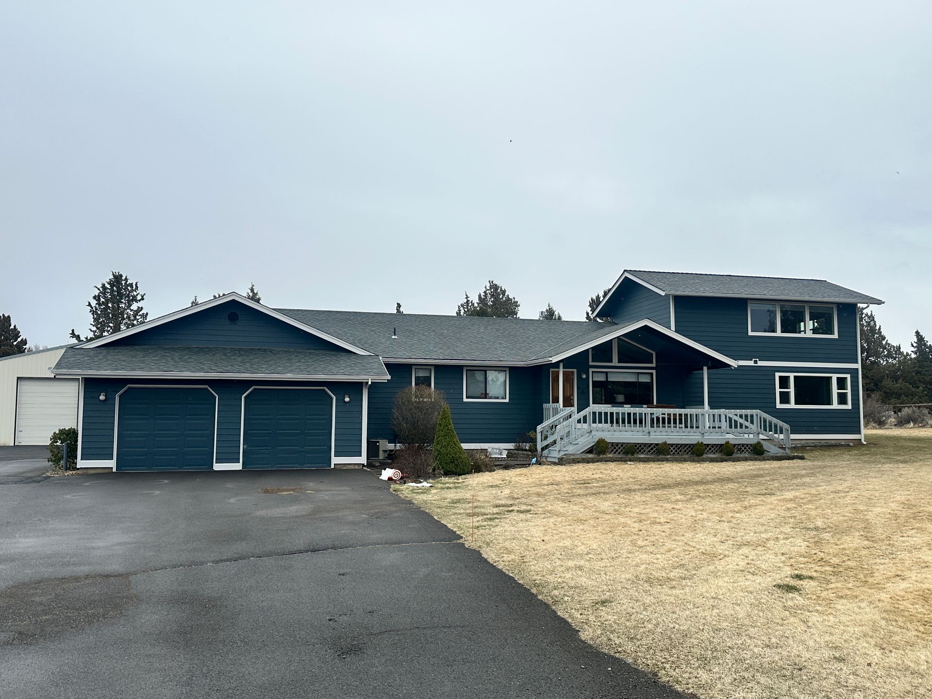 A large blue house with a gray roof is sitting on top of a lush green field.