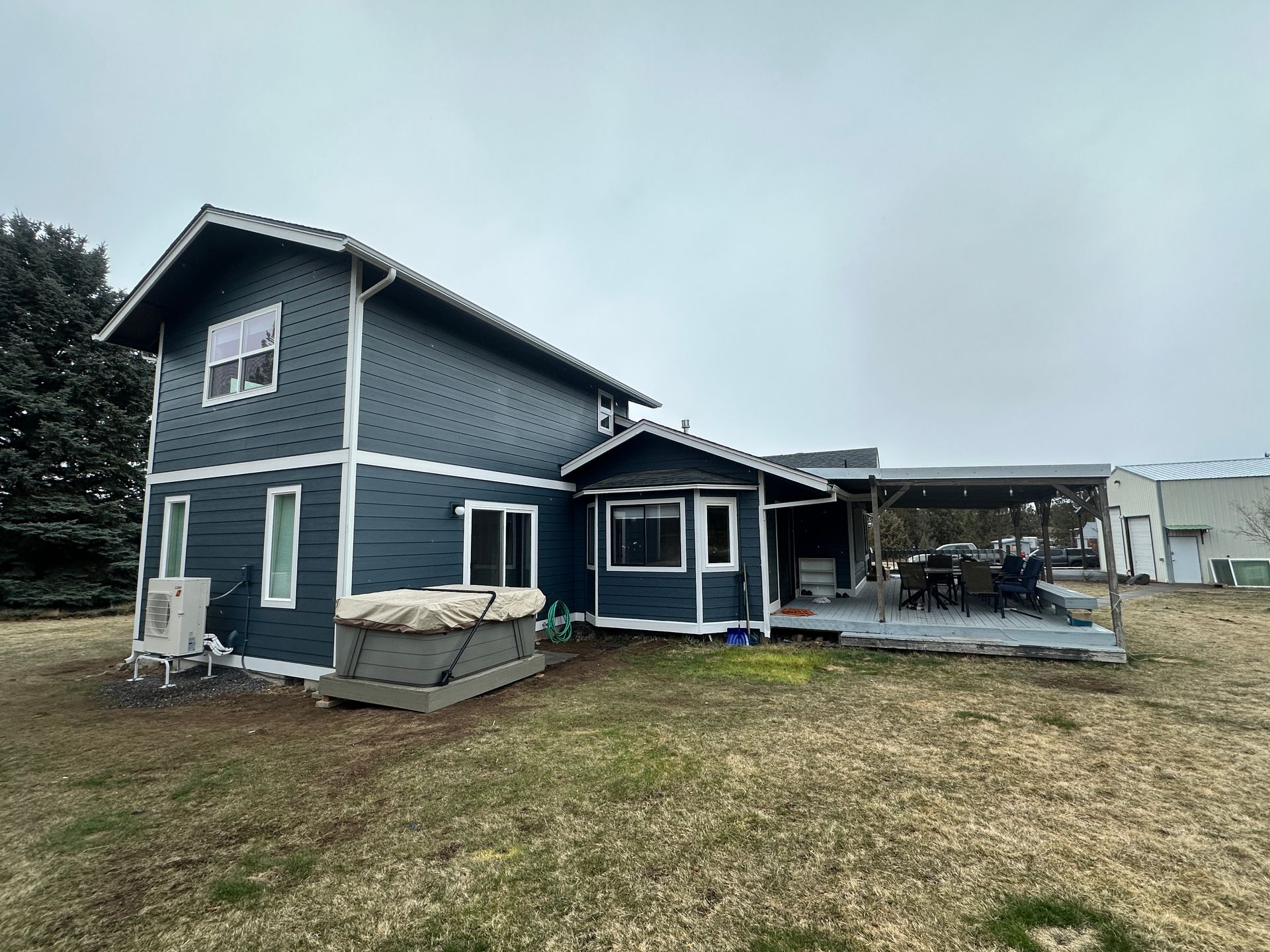 A large blue house with a porch and a hot tub in the backyard.