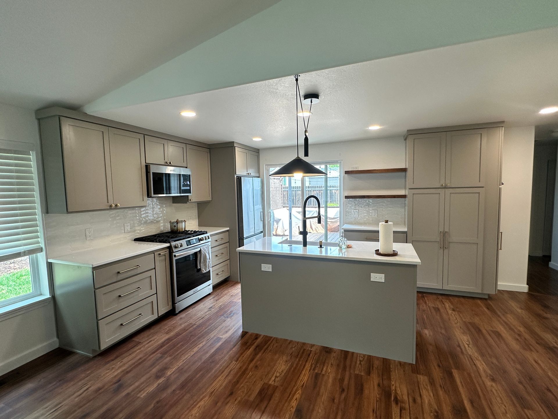 A kitchen with gray cabinets , stainless steel appliances , and a large island.